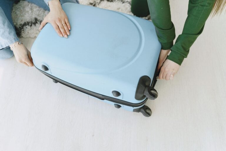 Unrecognizable female friends in casual clothes sitting on floor with fluffy carpet and opening suitcase together while preparing for journey and adventure